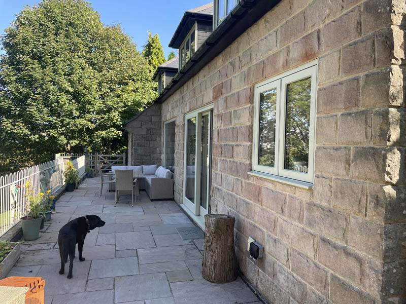 long view of timber windows in a stone cottage in matlock with a friendly dog on the patio